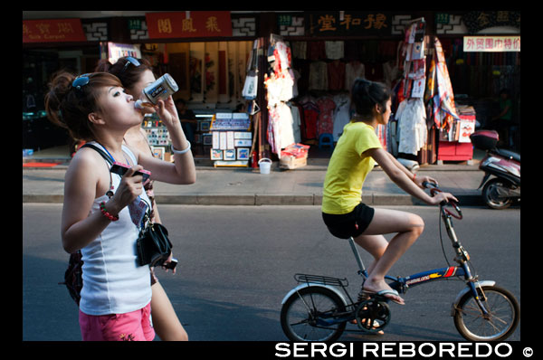 Caminar niñas y chica con una bicicleta por las tiendas pequeñas en la Ciudad Vieja, Shanghai, China. La ciudad vieja de Shanghai, Shangh? I L? O Chengxi? Ng, también conocido anteriormente como la ciudad china, es el núcleo urbano tradicional de Shanghai, China. Su límite se definía por una muralla defensiva. La Ciudad Vieja fue el asiento de condado para el antiguo condado de Shanghai. Con el advenimiento de las concesiones extranjeras en Shanghai, la ciudad vieja se convirtió en sólo una parte del núcleo urbano de Shanghai, pero continuó en las décadas por ser la sede de la autoridad de China en Shanghai. Las características notables incluyen el Templo del Dios de la Ciudad, ubicado en el centro de la Ciudad Vieja y está conectado con el Jardín Yuyuan. Con la excepción de dos secciones cortas, las paredes fueron demolidas en 1912, y una amplia avenida circular construida sobre la antigua muralla y el foso: la mitad sur se llamó el "Zhonghua Road" y la mitad norte de la "Minguo Road" (juntos haciendo arriba "Zhonghua Minguo", o "República de China" en chino). (La mitad norte pasó a llamarse "Renmin Road" ("Camino del Pueblo") en 1950 por el nuevo gobierno comunista de Shanghai). La Ciudad Vieja fue durante décadas en gran parte colindante con el antiguo Distrito Nanshi, que ahora es parte de distrito de Huangpu.