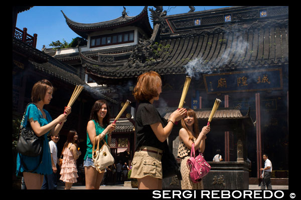 God Temple and pagoda, buddhist temple in Shanghai, burning joss sticks, incense. A women prays and laughs at Chenghuang Miao or City God Temple in Yu Yuan Gardens bazaar Shanghai, China. Located next to the Yuyuan Garden and also known today as the Yu Garden Market, the City God Temple (Chenghuang Temple) was built in the fifteenth century during the Ming Dynasty. Originally a temple built to honor the Han statesman Huo Guang (68 B.C.) The City God Temple is a Taoist temple which is composed of many halls such as the Grand Hall, Middle Hall, Bedroom Palace, Star Gods Hall, Yama Palace, Xuzhen God Hall. The temple had an area of more than 10,000 square meters including two gardens: West Garden (Yuyuan Garden) and East Garden. The City God Temple has a great influence on the residents of Shanghai. The religious festivals of the temple are considered to be the festivals for all Shanghai people.  Especially when the Sanxun festival (a day when the City God start to inspect his people) comes, nearly all people will come to the Temple to burn incense and worship the God, while all shops inside or close by would hang red lanterns to celebrate the festival. In addition, some folk arts, like cockfight, penmanship performance and acrobatics, are fairly attractive.