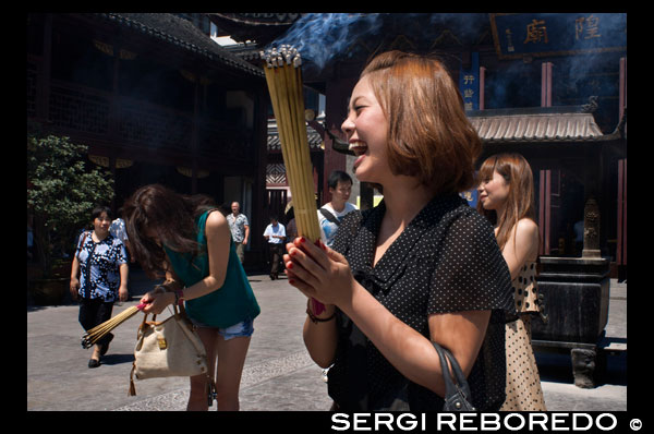 God Temple and pagoda, buddhist temple in Shanghai, burning joss sticks, incense. A women prays and laughs at Chenghuang Miao or City God Temple in Yu Yuan Gardens bazaar Shanghai, China. Located next to the Yuyuan Garden and also known today as the Yu Garden Market, the City God Temple (Chenghuang Temple) was built in the fifteenth century during the Ming Dynasty. Originally a temple built to honor the Han statesman Huo Guang (68 B.C.) The City God Temple is a Taoist temple which is composed of many halls such as the Grand Hall, Middle Hall, Bedroom Palace, Star Gods Hall, Yama Palace, Xuzhen God Hall. The temple had an area of more than 10,000 square meters including two gardens: West Garden (Yuyuan Garden) and East Garden. The City God Temple has a great influence on the residents of Shanghai. The religious festivals of the temple are considered to be the festivals for all Shanghai people.  Especially when the Sanxun festival (a day when the City God start to inspect his people) comes, nearly all people will come to the Temple to burn incense and worship the God, while all shops inside or close by would hang red lanterns to celebrate the festival. In addition, some folk arts, like cockfight, penmanship performance and acrobatics, are fairly attractive.