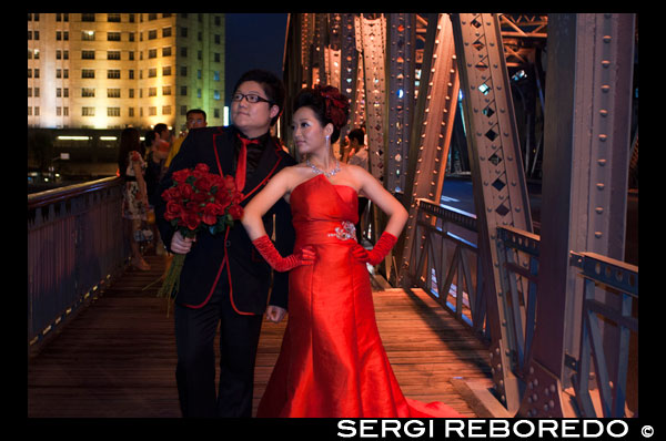 Wedding Photography at Garden bridge shanghai. Suzhou Creek, Waibaidu (Garden) Bridge, illuminated at night, Shanghai, China. The Waibaidu Bridge, Wàibáidù Qiáo, called the Garden Bridge in English, is the first all-steel bridge, and the only surviving example of a camelback truss bridge, in China. The fourth foreign bridge built at its location since 1856, in the downstream of the estuary of the Suzhou Creek, near its confluence with the Huangpu River, adjacent to the Bund in central Shanghai, connecting the Huangpu and Hongkou districts, the present bridge was opened on 20 January 1908. With its rich history and unique design the Waibaidu Bridge is one of the symbols of Shanghai. Its modern and industrial image may be regarded as the city's landmark bridge. On 15 February 1994 the Shanghai Municipal Government declared the bridge an example of Heritage Architecture, and one of the outstanding structures in Shanghai. In an ever-changing metropolis, the Waibaidu Bridge still remains a popular attraction, and one of the few constants in the city skyline. Before bridges were built over the Suzhou Creek (then known as the Wusong River), citizens had to use one of three ferry crossings: one near Zhapu Road, one at Jiangxi Road, and one near the mouth of the Suzhou River. These crossings (du in Chinese) were the only way to ford the river, until the construction of a sluice gate built in the Ming Dynasty, later known as "Old Sluice", where the current Fujian Road bridge is located. During the Qing Dynasty, another sluice bridge ("New Sluice") was constructed during the reign of Emperor Yongzheng (1723–1735), near the location of today's Datong Road bridge. With Shanghai becoming an international trade port through the Treaty of Nanjing in 1842, and foreign powers being granted concessions in the city, traffic between both sides of Suzhou River soared in the 1850s, increasing the need for a bridge close to the mouth of the river.
