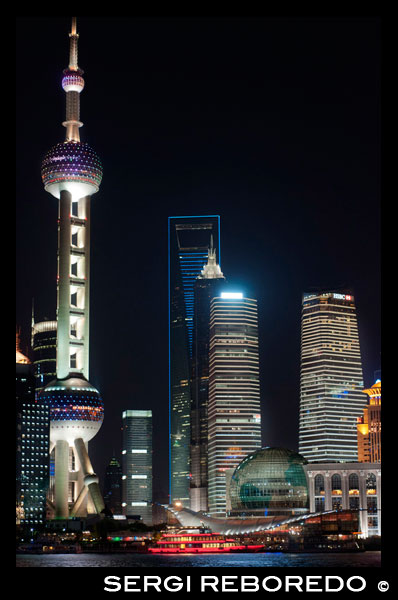 Pudong Skyline, by night, Shanghai, China. Skyline of Pudong as seen from the Bund, with landmark Oriental Pearl tower and Jin Mao tower, Shanghai, China. The word "bund" means an embankment or an embanked quay. The word comes from the Persian word band, through Hindustani, meaning an embankment, levee or dam (a cognate of English terms "bind", "bond" and "band", and the German word "Bund", etc.). It is thus named after the bunds/levees in Baghdad along the Tigris, when the Baghdadi Jews such as the prominent Sassoon family settled their business in Shanghai in the 19th century and built heavily on the bund on the Huangpo. In these Chinese port cities, the English term came to mean, especially, the embanked quay along the shore. In English, "Bund" is pronounced to rhyme with "fund". There are numerous sites in India, China, and Japan which are called "bunds" (e.g. the Yokohama Bund). However, "The Bund", without qualification as to location, usually refers to this stretch of embanked riverfront in Shanghai. The Chinese name for the Bund is unrelated in meaning: it means literally the "outer bank," referring to the Huangpu River, because this part of the riverfront was located farther downstream than the "inner bank" area adjacent to the old walled city of Shanghai. The Shanghai Bund has dozens of historical buildings, lining the Huangpu River, that once housed numerous banks and trading houses from the United Kingdom, France, the United States, Italy, Russia, Germany, Japan, the Netherlands and Belgium, as well as the consulates of Russia and Britain, a newspaper, the Shanghai Club and the Masonic Club. The Bund lies north of the old, walled city of Shanghai. It was initially a British settlement; later the British and American settlements were combined in the International Settlement. Magnificent commercial buildings in the Beaux Arts style sprung up in the years around the turn of the 20th century as the Bund developed into a major financial center of East Asia. Directly to the south, and just northeast of the old walled city, the former French Bund (the quai de France, part of the Shanghai French Concession) was of comparable size to the Bund but functioned more as a working harbourside. 