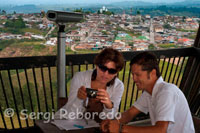 Dos turistas en el Mirador de Filandia. El pequeño pueblo de Filandia se divisa detrás de ellos. Circasia, Pereira, Salento, Quimbaya, Armenia y los municipios de Caicedonia, Cartago, Ulloa y Arabia, del Valle del Cauca son algunas de las localidades que turistas y habitantes de Filandia pueden apreciar al escalar cerca de 19 metros de altura que tiene el mirador del ecoparque Colina Iluminada. Con sólo 3 mil pesos y una buena disposición para subir escaleras, los visitantes disfrutarán de variados y hermosos paisajes, una de las maravillas quindianas que integran el turismo ecológico. Desde la parte más alta de la estructura que fue elaborada en mangle, chanú y zapán se observa un espejo de agua elaborado en forma de mariposa y con vitrales de colores, como un reconocimiento a las miles de especies de este tipo que se evidencian en la zona. Asimismo, desde allí no sólo se permite una vista territorial sino la opción de distinguir detalladamente la fauna y la flora a una escala de gran altura, además de brindarle al visitante la oportunidad de observar los límites con las municipalidades vecinas. Quienes deseen conocer este nuevo atractivo turístico y viajen desde Armenia deben dirigirse por la vía hacia Pereira tomando la autopista del Café, recorrido que dura cerca de 20 minutos. De allí se gira en el sector conocido como Cruces para hacer ingreso a la parte rural de dicho municipio. Después de pasar el parque principal se busca la carretera que conduce a Quimbaya y en sólo cinco minutos se podrá vislumbrar una imponente obra de la arquitectura que está abierta todos los días desde las 9:00 de la mañana hasta las 6:00 de la tarde.  Proyecto eco parque La iniciativa con la que fue concebida el ecoparque mirador Colina Iluminada fue la realización de un gran proyecto turístico con aspectos representativos de la región. Aunque por el momento sólo está lista la primera fase, para un futuro se tiene pensando ejecutar ocho núcleos allí. Parqueaderos, portería con taquilla, cubículo para la vigilancia, plaza de banderas, edificio administrativo, talleres, servicios sanitarios y un paraninfo o teatro al aire libre para la presentación de manifestaciones culturales, así como la Estancia del Arriero, el jardín botánico en selva de niebla, aulas didácticas, un vivero, eras de cultivo, invernadero en guadua y madera con tapa de vidrio, umbráculo —cobertizo con cubierta en Zaram para resguardar la flora de las inclemencias del tiempo— y el sendero botánico con puentes, estancias, jardines nativos y otros son los primeros aspectos que presenta este parque. Además se tendrán rampas arqueológicas, que mostrarán la riqueza cultural ancestral de pueblos como los Quimbayas y los Pijaos, un edificio social recreativo con cafetería, servicios complementarios, salón de juegos, e infraestructura para juegos infantiles relacionados directamente con el tema arqueológico, la plaza de la cultura de la música que estará elaborada en bambú, guadua y maderas tropicales, bóveda celeste, planteada en las mismas especies y con amarres en bejuco. Asimismo, una laguna artificial, con esculturas móviles recreativas accionadas por fuentes alternativas de energía, como la solar, la eólica, el gas o el agua.