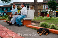 Ritmo sosegado en la Plaza central de la población de Filandia. Quindío. Filandia es otro de los pueblos predilectos por los visitantes debido a su tranquilidad y a la bonita arquitectura de la colonización antioqueña. La historia dice que don Felipe Meléndez, viejo colonizador, fundó el poblado en compañía de varios amigos y lo bautizó con la mezcla del latín fila (hija) y el inglés landia (Andes). Filandia: hija de los Andes. Se encuentra al norte del departamento por la Autopista del Café, de la que hay que desviarse a la izquierda en el km 20 para luego tomar una vía pavimentada y angosta de unos 7 km. Este último tramo se hace entre fincas y las reservas naturales de Bremen y Barbas, que  a la vez crean un entorno paisajístico muy llamativo por su verdor y fertilidad. El lugar está dispuesto en una meseta, ubicación desde donde se aprecian varias de las municipalidades limítrofes. Este destino ofrece también como encanto el carácter amable de los pobladores, muchos de ellos trabajadores de los cultivos de café, primer producto del municipio y motivo forjador de la cultura que se vive en todos sus rincones. Muchos de estos campesinos, al terminar sus jornadas, se congregan en la plaza y en los establecimientos públicos para compartir experiencias con tertulianos de adentro y de afuera. 