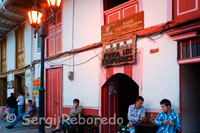 Fonda de los compadres. Algunos bares de Salento. Quindío. Salento está metido entre montañas cafeteras, palmas de cera, ríos transparentes y la niebla que en lo alto expulsan las cimas nevadas. Es un lugar armonioso para andarlo sin premura y con la certeza de que todo cuanto lo conforma tiene su motivo y su razón, esto hablando de las casas, la iglesia y todas las construcciones del casco urbano; los atractivos naturales, son regalos de la vida que no se explican, y han comenzado algunos kilómetros más abajo donde se desprende el camino de acceso en la Autopista del Café. Ese desvío a la derecha se interna por la ruta curvilínea del valle frondoso formado por el río Quindío; y por los lados donde este se descubre aún claro, aparece el corregimiento de Boquía, un anticipo de lo que está por venir. En ese caserío sobre el borde de la carretera, los primeros parroquianos gentiles y algunas típicas posadas turísticas, sencillas pero envueltas de verdor. Estos lugares de aposento están allí porque es  necesaria la estación y el resguardo para entrar en comunión con el entorno, las personas y el dejo cálido de su voz, los árboles teñidos de frutos, las estancias tranquilas que elevan a la ensoñación. Salento se empieza a vivir con todos los ingredientes de una vida tan natural como el verde que emana de la tierra y las aguas que bajan por las lomas. Y de nuevo el viajero está puesto en los caminos del municipio, allí por la Calle Real y otras están las demás posadas turísticas. Las del armazón emulado de la colonización antioqueña, cuyos rincones de bahareque, guadua y flores son cómplices de mariposas y pájaros que en  desbandada llegan a alegrar los días. Este espectáculo es para apreciar en los ratos de descanso o en los primeros momentos de la mañana, porque afuera hay mucho qué hacer: en la plaza central, entre la oferta artesanal y gastronómica de la Calle Real, en el mirador al final de la larga escalera o en el majestuoso valle de Cocora.