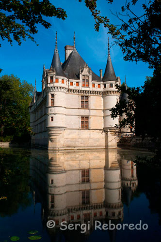 AZAY LE RIDEAU, UNO DE LOS EXITOS DEL RENACIMIENTO. Vista lateral del castillo. Varios kilómetros de bicicleta y llegamos a orillas del río Indre, donde rodeado de vegetación se alza este majestuoso castillo paradigma del Renacimiento.   Las aguas del río prácticamente rodean la fachada de esta fortaleza, quedando reflejada en sus aguas de una manera casi simétrica.  Su historia se remonta a la época romana, siendo fundamental posteriormente, en la Edad Media dónde desempeñó un papel militar de vigilancia sobre el Valle del Indre. Balzac describió esta pequeña joya como “un diamante tallado”, engrazado en el Indre”. Un romanticismo envuelve sus alrededores, en los que es posible pasear por extensas zonas verdes colindantes, y observar como una damisela vestida para la ocasión explica a los escolares venidos de lugares remotos de Francia la historia del “Hijo del diablo”, tal y como apodaban a Rideau d’Azay, el señor feudal que poseyó el castillo en el siglo XII. 