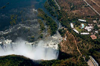 Vistas aéreas de las Cataratas Victoria. Cataratas Victoria presentan una espectacular vista del imponente belleza y la grandeza en el río Zambezi, que forma la frontera entre Zambia y Zimbabwe. Fue descrito por el Kololo tribu que vivía en la zona en la década de 1800 como "Mosi-oa-Tunya" - "El humo que truena". En términos más modernos Victoria Falls es conocida como la mayor cortina de agua que cae en el mundo. Columnas de aerosol se pueden ver desde kilómetros de distancia ya que, en el apogeo de la temporada de lluvias, más de quinientos millones de metros cúbicos de agua por minuto caen en picado sobre el borde, en una anchura de casi dos kilómetros, en un barranco de más de cien metros a continuación. La amplia, acantilado de basalto sobre la que el trueno caídas, transforma el Zambezi desde un plácido río en un torrente feroz corte a través de una serie de gargantas espectaculares.