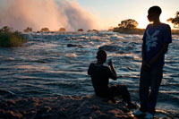 Turistas nacionales visitan las Cataratas Victoria . Estas son algunas de las cascadas más espectaculares del mundo. El río Zambezi , que es más de 2 km de ancho en este punto, se hunde estrepitosamente por una serie de gargantas de basalto y levanta una bruma iridiscente que se pueden ver más de 20 km. El Mosi-oa-Tunya/Victoria Falls es mayor de situación del mundo de la caída del agua y significativo en todo el mundo por sus características geológicas y geomorfológicas excepcionales y los procesos de formación del suelo activas con gran belleza atribuida a las cataratas , es decir, la pulverización , la niebla y el arco iris. Este establecimiento transfronterizo se extiende sobre 6860 hectáreas y comprende 3.779 hectáreas del Parque Nacional de Mosi -oa- Tunya (Zambia ) , 2.340 hectáreas de Parque Nacional de las Cataratas Victoria (Zimbabwe ), 741 hectáreas de la franja ribereña del Zambezi National Park (Zimbabue ) . Una franja ribereña del Parque Nacional Zambezi extiende 9 km al oeste a lo largo de la margen derecha del Zambeze y las islas en el río son todos dentro del parque en cuanto a la palma y las Islas de Kandahar , con las Cataratas Victoria es una de las principales atracciones.