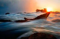 Sunset in the Victoria Falls. The Victoria Falls or Mosi-oa-Tunya (Tokaleya Tonga: the Smoke that Thunders; the 'i' is silent) is a waterfall located in southern Africa on the Zambezi River between the countries of Zambia and Zimbabwe. The falls are believed to be the largest in the world in terms of the volume of water that passes through. These ancient and truly spectacular Falls were first made known to the outside world in 1855 by Scottish explorer extraordinaire, David Livingstone. Livingstone had been attempting to find a route to the East Coast of the African continent. Travelling south east from Luanda to Sesheke, he encountered this most magnificent waterfall and renamed it the Victoria Falls after the British Monarch, Queen Victoria. Livingstone was led to the Falls by the Makalolo tribes people in a dug-out canoe. During the Jurassic Period (150-200 million years ago), volcanic activity resulted in thick basalt deposits covering large parts of Southern Africa. 