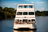 Cruise along the Victoria Falls aboard the " African Queen".  Other boats sailing in the Zambezi River. This is the “Lady Livingstone” boat.  River Cruises. Few places offer the dramatic sunsets that you'll find on the Zambezi River with plumes of spray and wildlife completing the scene. The sunset cruise on the Zambezi River is a definite must on any trip to Victoria Falls. Relax with a sundowner and snacks as you gaze out onto the banks of the river. Have your camera ready to capture one of the most amazing sunsets in Africa. You'll be sure to spot wildlife animals as they come down to the river for a drink after a hot day in the Zambezi National Park (Zimbabwe) and the Mosi-oa-Tunya National Park (Zambia). Sightings of elephant, giraffe and other resident game are common. There's always an abundance of hippos and crocodiles. Birdlife is superb and the Fisheagles will usually fill the scene with their calls. Cruises are available daily on request for breakfast, lunch, sunset and dinner and last for approximately 2 to 3 hours.  Transfers from hotels in both Livingstone and Vic Falls town are included. (*Park Fees excluded - applicable in Zimbabwe) 