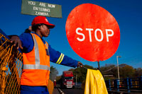 A woman controls the traffic between Zambia and Zimbabwe.  A STOP sign indicates that we are entering Zambia. Today one of the Victoria Falls Bridge's main attraction are historical guided tours focusing on the construction of the bridge and which include a walking tour under the main deck. On the Zambian side there is a small museum about the bridge which is free to enter and contains cafe selling refreshments. Also located on the bridge is the Shearwater 111 meters (364 ft) bungee jump including a bungee swing and zip-line. Concerns about safety of the attraction were raised in late 2011 after the bungee's cord snapped and a young Australian woman fell 24 meters (79 ft) into the fast flowing river with many crocodiles. The bridge was originally referred to as the Great Zambesi or Zambezi bridge, later becoming known as the Victoria Falls Bridge. 