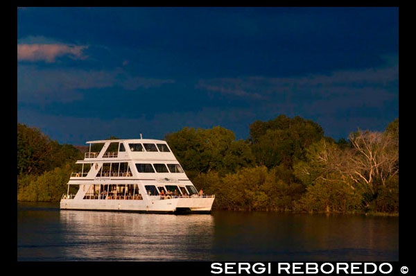 Crucero a lo largo de las Cataratas Victoria a bordo del "African Queen" . Otros barcos que navegan en el río Zambezi . Este es el barco "Lady Livingstone " . El recientemente construido señora Livingstone famoso conocido como " La joya del Zambezi " tiene una capacidad de 144 pax . Los huéspedes son recibidos en sus respectivos hoteles / Lodges y transferidos al David Livingstone Safari Lodge & Spa . El crucero tiene lugar a lo largo de la frontera del río del Parque Nacional de Mosi -Oa- Tunya , el tiempo total de crucero es de aproximadamente 2 horas. Durante el crucero , los clientes tienden a ver hipopótamos , cocodrilos y algunos buenos pájaros . Otros posibles avistamientos de juego son elefantes, jirafas , búfalos y dinero. Un experimentado guía acompaña a cada crucero y tiene buen conocimiento sobre la fauna y la historia local de la zona . Excelentes aperitivos fríos y calientes se sirven a bordo y el bar está bien surtido con los espíritus , buenos vinos , cervezas y refrescos. Bocadillos y bebidas están incluidas en el precio y se sirve durante todo el crucero . Pick up horarios son 16h00 en verano (agosto a abril) y 15h30 en invierno (mayo a julio). The Waterfront opera dos barcos de cruceros - "MV Makumbi " y el "MV Mambushi " . Además de nuestros cruceros al atardecer regulares , los barcos también están disponibles para eventos privados y se pueden reservar de forma exclusiva por encargo. El crucero es a lo largo de la frontera del río del Parque Nacional de Mosi -Oa- Tunya , alrededor Siloka isla y de vuelta al embarcadero Waterfront. Desde el barco , avistamiento de fauna silvestre que bajan al río a beber son comunes. También abundan los hipopótamos , cocodrilos y aves. Un experimentado guía acompaña a cada crucero y tiene buen conocimiento sobre la fauna y la historia local de la zona.