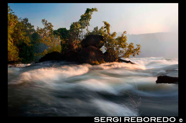 Posta de sol a les Cascades Victòria. Victoria Falls a la frontera entre Zimbabwe i Zàmbia té algunes de les més impressionants vistes que mai troba al continent africà, sinó del món. El full massiva de la caiguda de l'aigua i l'escuma que produeix és fascinant per dir el menys. El proper Parc Nacional de les Cascades Victòria i les ciutats de Victoria Falls i Livingstone ofereixen plaers addicionals per al visitant exigent. The Victoria Falls és una de les atraccions més populars al sud d'Àfrica, on es pot explorar la vida salvatge africana com ho va fer el Dr Livingstone fa tants anys. Arribar i sortir de Victoria Falls és una brisa com el Victoria Falls Airport s'acomoda vols des de Johannesburg, Windhoek, Harare i Bulawayo. Hi ha plans per ampliar la pista d'aterratge per acomodar avions més grans, que al seu torn podria significar vols directes de destinacions a l'estranger, com Europa i Amèrica. Hi ha serveis de transferència decents generalment organitzades per les lògies i el seu viatge ha de ser sa i estalvi. Les Cataractes Victòria té moltes característiques que et mantindrà entretingut i divertit. Piscina del Diable, al costat de Zàmbia és una de les coses més boges que mai es pot fer. En la mateixa vora de les Cascades Victòria hi ha una paret de roca que es crea un fons comú que es pot nedar en tant el corrent no és massa forta. Pot arribar al seu punt màxim a la caiguda de 108 metres a sota de la vora. És tan increïble com el seu nervi de demolició. The Victoria Falls i l'esprai produeix sosté un ecosistema que suporta diversos animals i plantes. Missioner escocès David Livingstone per primera vegada sobre les cascades Victòria, conegut com Mosi-oa-Tunya, quatre anys abans que arribés allà. L'àrea era un lloc sagrat per al Batoka i altres tribus locals. El 17 de novembre de 1855, Cap Sekeletu del Makololo remar Livingstone a una illa en el riu Zambeze, coneguda com a illa de la cabra. Encara que l'aigua estava baixa en el moment, Livingstone encara se sentia un "tremolor de la por" quan es va acostar a la paret de l'aerosol. Mirant cap avall en l'abisme batut baix ha d'haver estat una experiència heartstopping (vostè encara pot fer el seu camí a l'illa, que ara es diu l'illa de Livingstone, des del costat de Zàmbia durant l'estació seca). Els rumors que un portuguès va avançar tenen poca evidència. Livingstone va descriure el que va veure: ". Ningú no pot imaginar la bellesa de la vista de tot el que s'ha vist a Anglaterra Mai abans s'havia vist per ulls europeus, però les escenes tan boniques s'ha d'haver mirat sobre per àngels en el seu vol".