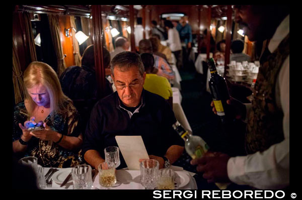  Inside the restaurant railway carriage of Royal Livingstone Express luxury train. The ambiance of the dining carriage offers more than warm elegance. The sash windows allow for panoramic views of the passing parade, while the incandescent lighting adds intimate warmth from individual lamps on each table gently illuminating the beautifully detailed wooden interiors. The silver cutlery, crystal glassware and damask linen provide the ideal backdrop to the exquisite cuisine created by the Royal Livingstone Hotel chefs.  The journey begins when you're collected from the Royal Livingstone Hotel at 17h00 and transferred to the old Mulobezi Line Offices, where guests board the immaculate vintage first class Lounge carriage.  There are two dining cars with a seating capacity for 92 passengers and a fully equipped kitchen car to produce a 6-course gourmet dining experience. From departure the train moves directly onto the old Mulobezi Line, which has also been restored. It was once the largest privately owned railway network in the world and was set up by the Zambezi Sawmills in 1916.  The journey commences through Dambwa suburb towards the Mosi-oa-Tunya National Park, running parallel to the Zambezi River. Guests have the opportunity to catch glimpses of white rhino, buffalo, elephant and other wildlife. From there, the train crosses out of the Mosi-Oa-Tunya National Park over the Sinde River and comes to pause some 17 kilometres from Livingstone. By this time darkness would have descended on the Zambezi Valley and guests will be invited to dinner by the train manager in the dining cars. The train will then slowly push back to the Sinde 'run around' to afford the locomotive driver a good view of any obstacles in his path for the return journey in darkness, including of course elephants! The journey finishes back at the old Mulobezi Siding at approximately 21h30.  The companies involved in the resurrection process are Sun International Zambia, Bushtracks Africa, and the National Heritage Conservation Commission.