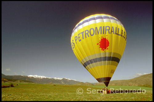 Travesía por el parque en globo. Nuestro viaje comienza en un pueblo situado al norte del Parque Natural Cadí-Moixeró llamado Bellver de Cerdaña.  Es el municipio de la Cerdaña que integra mayor superficie del Parque y en su geografía serpentean las aguas del río Segre. Al llegar al punto de reunión, un bar situado a los pies de la Nacional 260, Miquel Mesegué, el piloto del globo aerostático, ya esta esperándonos para trasladarnos en la furgoneta que remolca la enorme cesta y las telas del globo al lugar de salida.  La mañana es soleada, ni una sola nube asoma por el horizonte. Desplegamos las telas en un descampado próximo y los quemadores de gas propano comienzan a inundar el interior de éstas de aire caliente. Lentamente, el enorme balón de color amarillo va cogiendo forma hasta llenar los 9000 metros cúbicos de aire que caben en su interior, mientras la cesta empieza a moverse como si tuviera prisa por empezar a volar. 