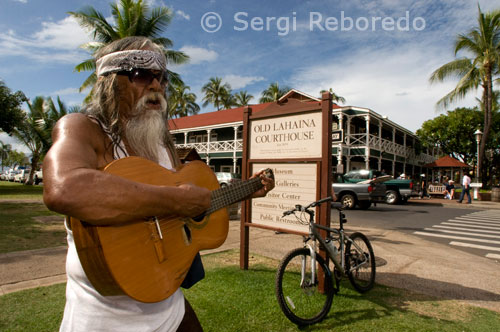 Tocando la guitarra cerca del emblemático y antiguo edificio Juzgado-prisión de Lahaina. Maui. Estas son totalmente diferentes de las olas tubo de California, que normalmente tienen una longitud de onda de 100.5 m (330 pies) y un período de alrededor de diez segundos. Cuando un tsunami alcanza las zonas de menor profundidad, puede bajar la marea y la energía de la gran ola se incrementa destruyendo todo a su paso. Arrecifes de coral, bahías, ríos, características del fondo oceánico y la bajada de marea pueden ayudar a modificar el tsunami en su aproximación a la costa. Las olas del tsunami rara vez rompen en la costa. Algunas veces pueden romper lejos de ésta. En ocasiones, el tsunami puede formar una ola pronunciada si avanza desde una zona profunda hacia una bahía o río. La primera ola puede no ser la más poderosa en la serie de olas. Algunas zonas costeras pueden no sufrir grandes daños, mientras que en otras, las olas pueden ser violentas y poderosas. La inundación puede extenderse tierra adentro 305 m (1.000 pies) o más, cubriendo extensiones de tierra no solamente con agua, sino con los desechos y restos que ésta acarrea. Las olas tienden a trasladar objetos y personas mar adentro cuando se repliegan.