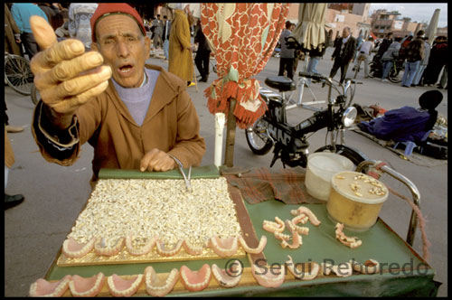 Vendedor de dientes en la plaza Djemaa el Fna. Rodeada de cafés y restaurantes con sus terrazas, es el punto perfecto para la contemplación de la vida que fluye por la plaza. Situada junto al zoco donde se puede encontrar casi cualquier cosa susceptible de ser comprada, tiene sus horarios y si por la mañana está poblada por puestos de zumo de naranja recien exprimido y tenderetes de aceitunas, frutos secos y dátiles, por la tarde, con la llegada de turistas y locales de paso empieza a llenarse con una mezcla de curiosos personajes: Narradores de cuentos se codean con aguadores, encantadores de serpientes, bailarines, adivinadores, escritores de cartas,, dentistas, ...que comparten espacio hacía el final de la tarde con decenas de restaurantes-chiringuitos,  identificados por números,  que hacen  las delicias de locales y foráneos.