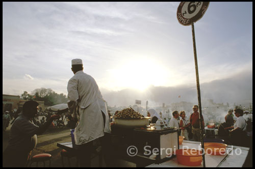 Marrakech. Plaza de Jemaa el Fna. or la tarde la cosa decae un poco para animarse de manera exponencial durante las primeras horas de la noche. Entonces, un mar de tenderetes de comida callejera ocupa el centro de la plaza y los más variopintos espectáculos de calle se desarrollan en sus alrededores. Contadores de cuentos, boxeadores aficionados, músicos ambulantes o funambulistas toman el lugar convirtiendo la Asamblea de los muertos en todo un festival a cielo abierto. Las linternas de gas y el humo de las cientos de parrillas aumentan la sensación de multitud entre gaitas, tambores, gritos y el ruido de un tráfico incesante que serpentea entre la multitud. Jemaá el Fna se vive a pie de calle, mezclándose con la gente y curioseando entre puestos y los corrillos que se forman en torno a los espectáculos callejeros. Pero conviene subir a alguna de las terrazas de los cafés que se localizan en la plaza para tener una visión de conjunto a vista de pájaro. La mejor opción es el Café Glacier, que permite una visión de más de 270 grados sobre el caos reinante. Para disfrutar de estas vistas sobre la multitud hay que consumir algo. Los tés a la menta y los pastelillos árabes del lugar son míticos.