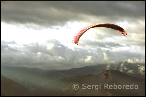 Volando en tandem. Parapente en Tierra Negra. Merida. Venezuela. Esa misma tarde salgo del centro de Mérida después de comer. La idea es hacer parapente en una montaña cercana. Después de 45 minutos de tortuoso recorrido, por fin habíamos llegado a Las González o al lugar más comúnmente llamado Tierra Negra. Nadie supo explicarme el porqué de este nombre, pero la cuestión es que la tierra no era ni mucho menos de color negra, sino de un tono rojo cobrizo que contrastaba enormemente con el azul electrizante del cielo. Nos encontrábamos en una enorme planicie a 1700 metros sobre el nivel del mar con unas fabulosas vistas del valle y del río Chama.   El parapente (contracción de paracaídas de pendiente) es un deporte nacido, a fines del siglo XX, por la inventiva de montañeros que querían bajar volando mediante un paracaídas desde las cimas que habían ascendido. El ala, y a veces todo el equipo, se llama así con el mismo nombre, parapente. La definición técnica sería algo así: planeador ligero flexible. Planeador porque no consta de motor y flexible porque no hay partes rígidas que compongan el ala, por lo que puede ser transportado en el maletero de un coche. El peso de todo el equipo, suele rondar los 25-30 kg aunque hay equipos para montaña con una masa aproximada de unos 8 kg . El piloto y ocasionalmente el pasajero de parapente estarán equipados con el equipo de seguridad obligatorio, cascos y paracaídas de emergencia y con diversos instrumentos electrónicos: variómetro o altivario, GPS y equipo de radio. Parapente biplaza.
