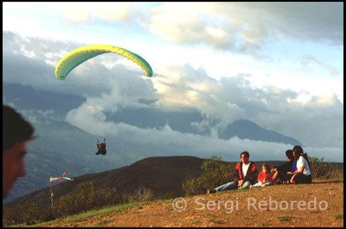 Algunos aficionados se acercan para ver volar los parapentes.  Parapente en Tierra Negra.  Venezuela. Uno a uno los parapentes fueron descendiendo por el valle. La suavidad con que planeaban era asombrosa. Los curiosos se habían colocado en lugares estratégicos de la ladera desde donde se podía divisar todo el espectáculo. Algunas familias estaban al completo, y sus hijos de corta edad eran los que más disfrutaban, eso sí, sin acabar de entender todas las explicaciones que sus padres les estaban dando sobre como un hombre podía mantenerse en el cielo tanto rato sin llegar a caerse. Para las gentes de Mérida este idílico paraje resultaba un lugar cautivador donde poder pasar el rato unidos merendando, mientras las vistas iban cambiando minuto a minuto como si de una película se tratase. Recomendación: debes comer algo liviano antes del vuelo.   Atuendo: Zapatos deportivos, pantalón largo y una chaqueta o suéter.  ¿Que es un parapente?   El parapente es un planeador ligero flexible, siendo la aeronave más ligera del planeta. Es un deporte de aventura que viene del siglo XX, por el invento de unos montañeros que querían bajar volando la cima de una montaña con un paracaídas.  Es fabricado con tejidos y materiales textiles, que no conforman ninguna estructura rígida.  Pesa menos que el piloto, permite despegar y aterrizar a pie, sin ningún impulso externo. 
